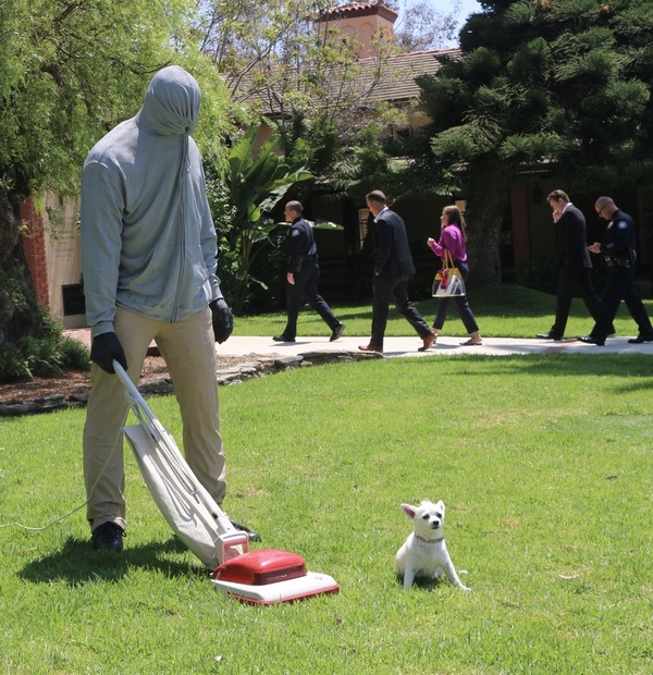 Hooded figure vacuuming the City Hall lawn as officers and staff walk into the building