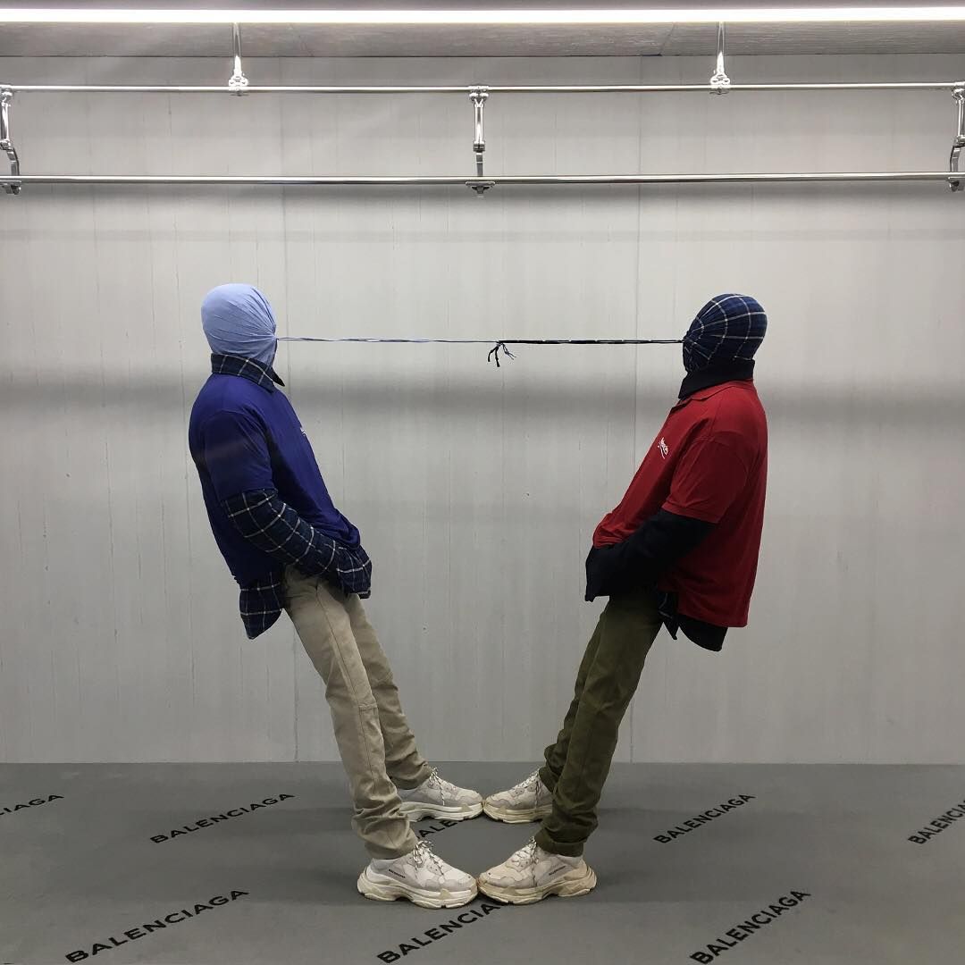 Two hooded figures leaning back, tethered head to head, Balenciaga